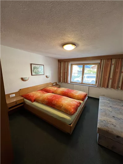 A simple room with two beds and colorful blankets. The window provides daylight and a view outside.