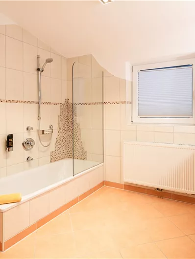 Ein modernes Badezimmer mit einer Badewanne und einer Dusche. Es ist hell und freundlich gestaltet, mit Handtüchern bereitgelegt.
