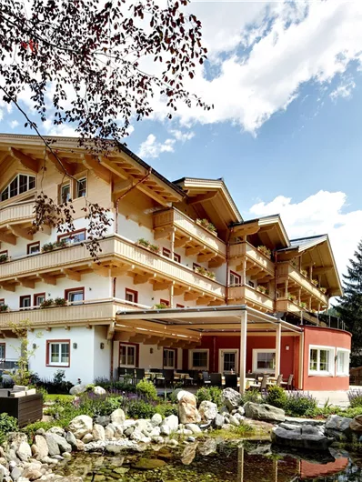 Ein gemütliches Hotel mit einem traditionellen österreichischen Architekturstil, umgeben von Bäumen und einer schönen Landschaft. Der Garten bietet eine entspannende Atmosphäre mit einem Teich und Spielplatz.