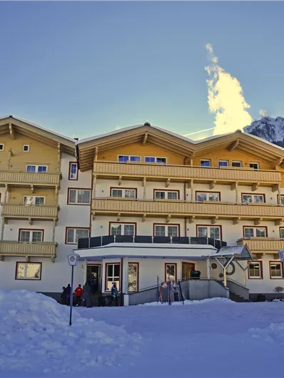 Ein gemütliches Hotel in den Alpen, umgeben von schneebedeckten Bergen. Der Himmel ist klar und die Sonne scheint.