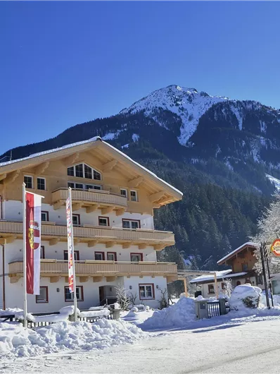Ein schönes Berglandhaus im Schnee mit blauen Himmel und umliegenden Bergen. Der Winterzauber schafft eine einladende Atmosphäre.
