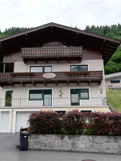 Een groot huis in alpine stijl met houtbekleding en balkon. Omgeven door groene heuvels en een rustige buurt.
