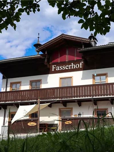 Ein gemütliches Landhaus mit einem Balkongeländer und Blumen im Garten. Der Himmel ist blau mit einigen Wolken.
