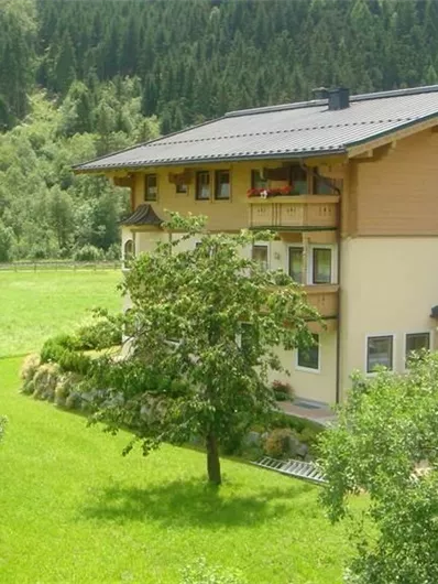 Een mooi huis omgeven door groene landschappen en bomen. Op de achtergrond zijn zachte heuvels en bossen te zien.