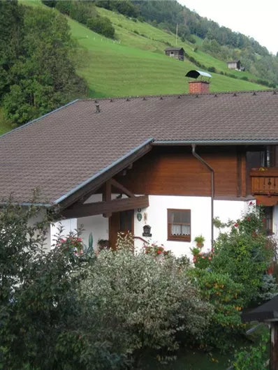 Een mooi huis in landelijke omgeving, omgeven door groene heuvels. Kleurige planten en bomen sieren de tuin.