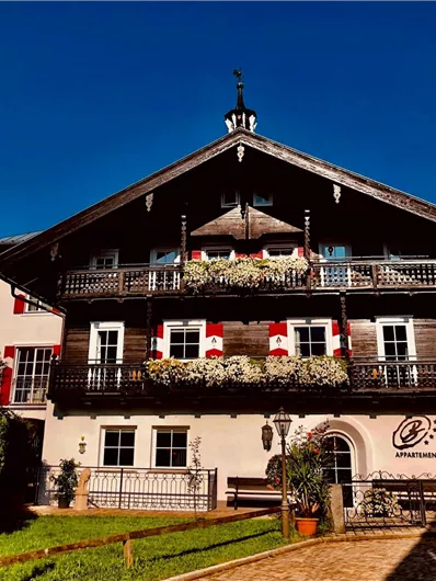 Ein traditionelles Alpenhaus mit schönem Holzbalustraden und blühenden Blumen. Der klare, blaue Himmel bildet einen tollen Kontrast zur Architektur.