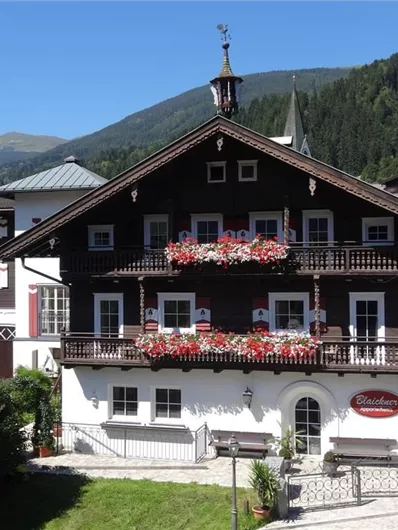 Ein traditionelles alpenländisches Haus mit Blumenkästen und einem schönen Ausblick auf die Berge. Die Fassade ist Holz gebaut und im typischen Stil der Region gehalten.