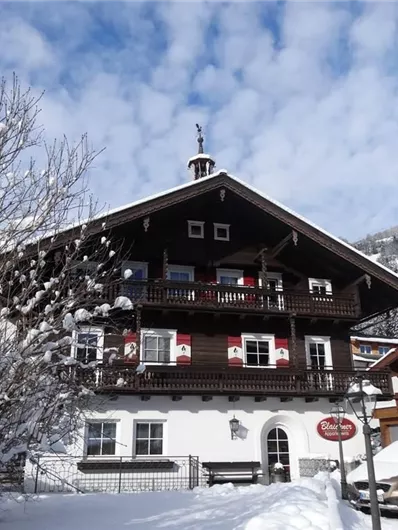 Een schilderachtig, traditioneel chalet in een sneeuwachtig winterlandschap. De omgeving is rustig met met sneeuw bedekte bomen en bergen op de achtergrond.