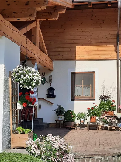 Een uitnodigende huisentree met houten veranda en veel bloemen. De omgeving is verzorgd en vriendelijk.
