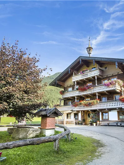 Een pittoresk houten huis met balkons, versierd met bloemen. Omringd door groene weiden en een blauwe lucht.