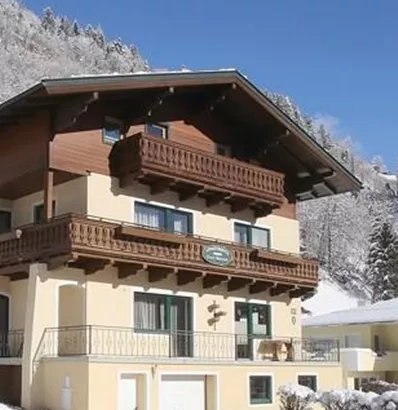 Een charmant gebouw in de sneeuw, omringd door met sneeuw bedekte bergen. De lucht is helder en blauw, wat een gezellige winteratmosfeer creëert.