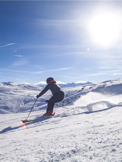 A skier is going down a snowy slope. The sky is clear and the sun is shining brightly.