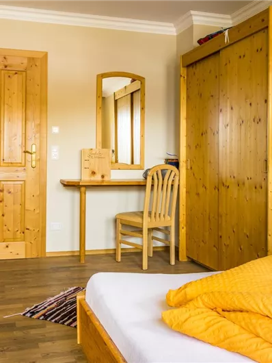 Een gezellig slaapkamer met houten meubels en een groot bed. Een tafel met stoel en een kast maken de kamer compleet.