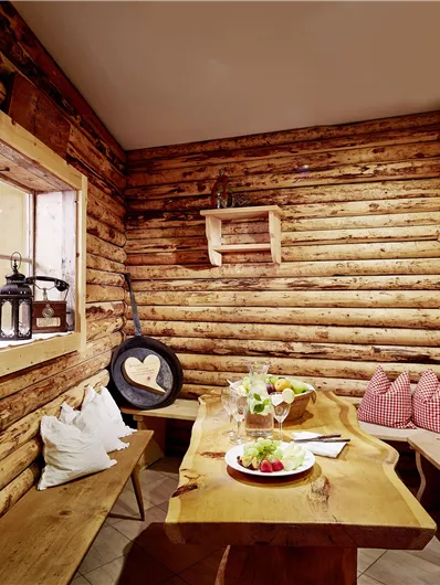 Een gezellige houten hut met een grote tafel en bankjes. Op de tafel ligt een mooi gedekte schotel met verse gerechten.