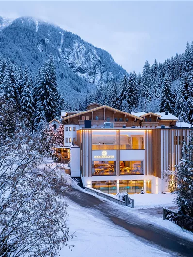 Ein modernes Gebäude im Schnee, umgeben von hohen, schneebedeckten Bergen. Die winterliche Szene vermittelt eine gemütliche Atmosphäre.