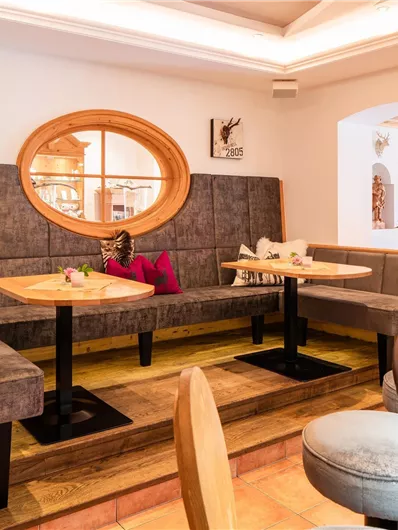 A cozy dining area with a bench and a round mirror. The walls are adorned with decorative animal horns.