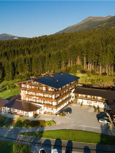 Ein charmantes Hotel umgeben von grünen Wäldern und Bergen. Die Anlage bietet großzügige Parkmöglichkeiten und eine einladende Architektur im alpinen Stil.
