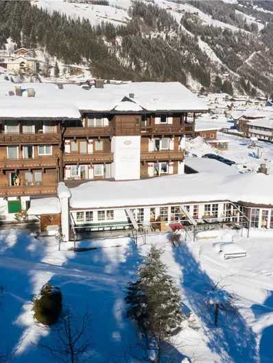 Ein gemütliches Hotel in einer schneebedeckten Landschaft. Die Umgebung besteht aus verschneiten Bergen und Bäumen.