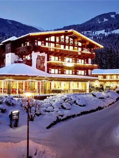 A cozy hotel in the mountains, surrounded by snow-covered landscapes. The lighting creates an inviting atmosphere at dusk.