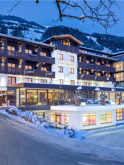 Een modern hotel in een besneeuwd landschap. De avondlucht is blauw en de lichten van het gebouw stralen vriendelijk.