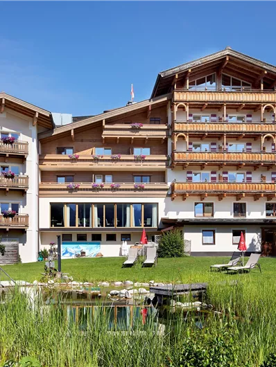 Een gezellig hotel met meerdere balkons en een mooie tuinlandschap. De lucht is blauw en de omgeving lijkt uitnodigend.
