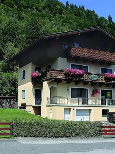 Een mooi huis met balkons, omringd door groene heuvels. Kleurrijke bloemen sieren de ramen, en de omgeving is rustig en uitnodigend.