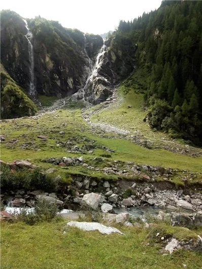 Een indrukwekkende waterval stroomt door een groene landschap met rotsen. Omringd door hoge bomen en bergen straalt de scène rust en natuurlijkheid uit.