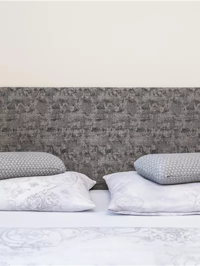 Een gezellige slaapkamer met een grijze hoofdbord en twee kussens. De beddengoed is licht en eenvoudig gehouden.