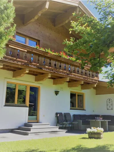 Ein gemütliches Holzhaus mit einem Balkon und einem gepflegten Garten. Der Außenbereich ist von Bäumen umgeben und lädt zum Entspannen ein.