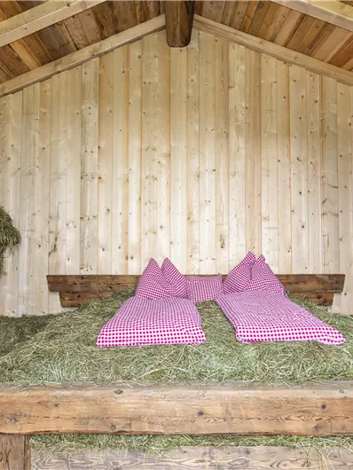Een gezellige kamer met houten wandbekleding en een bed van hooi. Twee roze kussens liggen op het bed, omringd door hooi-bundels.
