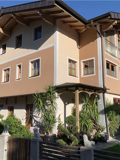 A modern multi-family house with a beige and orange paint job. Surrounded by plants and a well-kept garden.