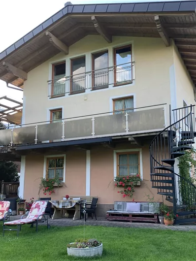 A modern house with a balcony and a spiral staircase. The garden is cozy with lounge chairs and beautiful plants.