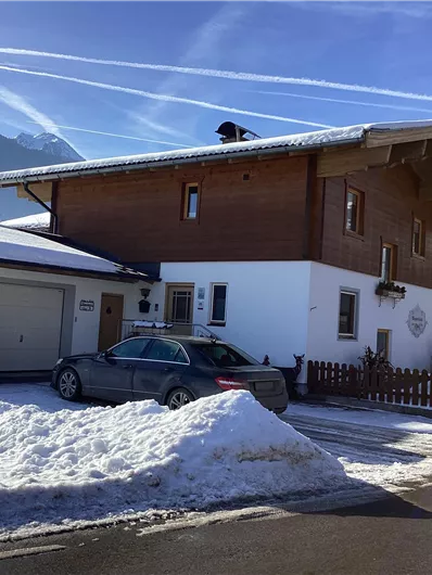 Ein charmantes Haus im Schnee mit Holz- und Weißtönen. Die Umgebung ist bergig und klarer Himmel ist zu sehen.
