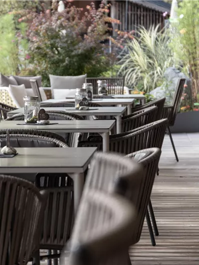 Ein modernes Restaurant mit eleganten Tischen und Stühlen. Die Terrasse ist grün gestaltet und lädt zum Verweilen ein.