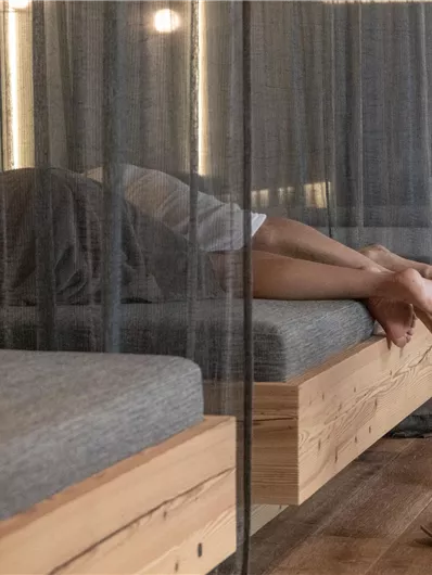 Eine entspannte Wellness-Atmosphäre mit Liegen und weichem Licht. Zwei Personen liegen hinter einem Vorhang und genießen ihre Ruhe.