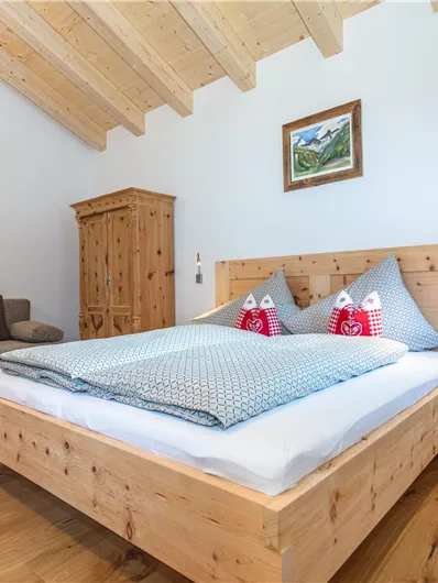 Een gezellige slaapkamer met een groot houten bed en een bank. Heldere muren en een mooie houten vloer creëren een ontspannen sfeer.