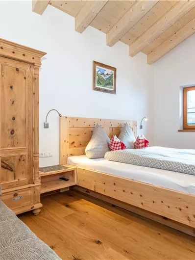 Een heldere slaapkamer met een tweepersoonsbed en een gezellige houten meubel. Grote ramen zorgen voor veel daglicht en een warme sfeer.