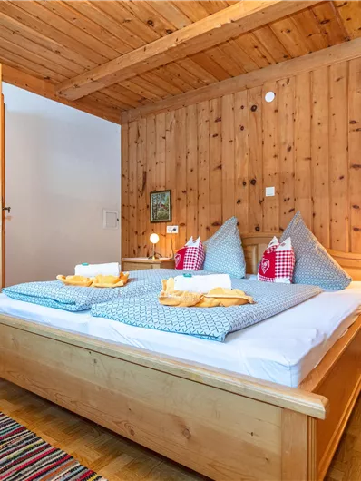 Een gezellige slaapkamer met houten wandbekleding en een groot bed. Op de achtergrond is een open keuken te zien.