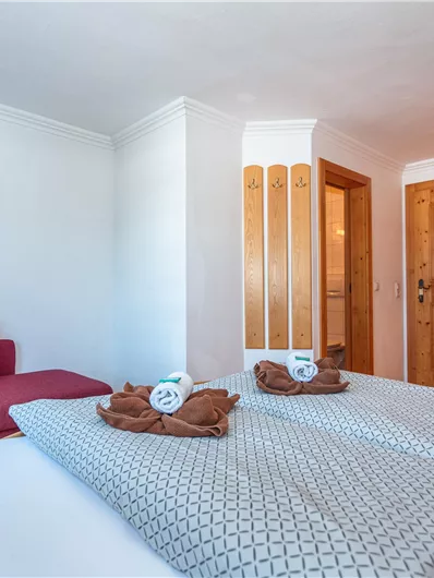 Een gezellige kamer met twee bedden, een televisie en een rode bank. De houten details en de warme kleuren zorgen voor een uitnodigende sfeer.