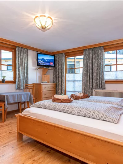 Een gezellig houten kamer met een tweepersoonsbed en een kleine tafel. De grote ramen laten veel licht binnen en bieden een ontspannen uitzicht.