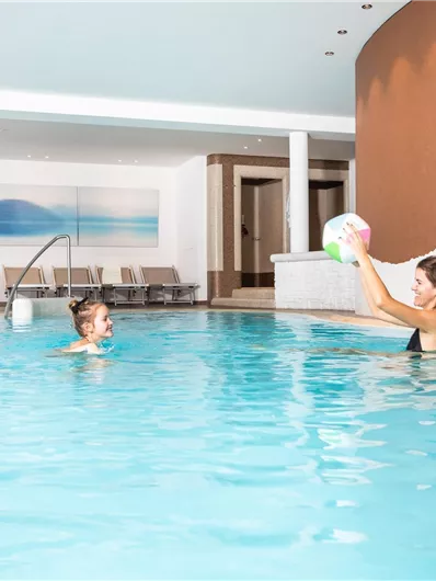Een binnenzwembad met helder water. Een vrouw speelt met een kind in het water.