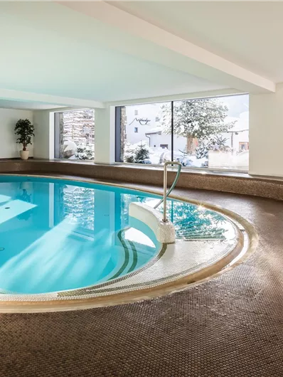 An elegant indoor pool with clear water and large windows offering a view of a snowy landscape. The room is bright and inviting, perfect for relaxing.