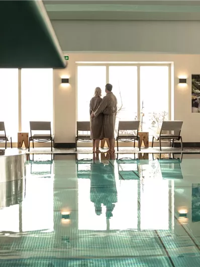 Ein eleganter Wellnessbereich mit einem Pool und Liegen. Zwei Personen stehen am Poolrand und betrachten den Raum.