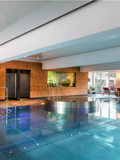 Ein modernes Schwimmbad mit glattem Wasser und Lichteffekten. Der Raum ist hell und einladend, mit Liegen und großen Fenstern.