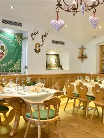 Een gezellige eetzaal met houtdecor en feestelijk gedekte tafels. Aan de muur hangt een groene banner en er zijn decoratieve elementen zoals geweien.