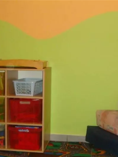 Een vrolijke kinderkamer met kleurrijke muren en een bed. Er is speelgoed en een kast voor het opbergen van spullen.