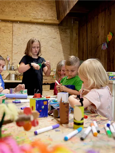 Eine Gruppe von Kindern bastelt gemeinsam in einem kreativen Raum. Auf dem Tisch liegen verschiedene Bastelmaterialien, während die Kinder eifrig daran arbeiten.