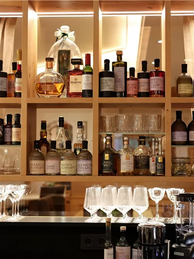 Eine elegante Bar mit einer Auswahl an Spirituosen und Gläsern. Die Regale sind warm beleuchtet und verleihen eine gemütliche Atmosphäre.