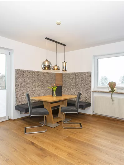 Een moderne keuken met een eettafel van hout. Grote ramen zorgen voor veel daglicht.