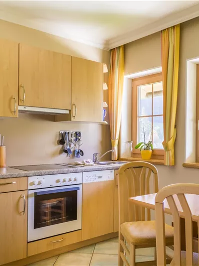 Een gezellige keuken met houten kasten en moderne apparaten. Twee ramen laten veel licht binnen en creëren een uitnodigende sfeer.